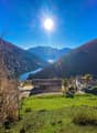 Green grass, two houses, mountains, lake, clear sky, sun