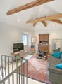 living room with wooden beams, gray couch, blue pillows, wooden desk, TV, wooden cabinet, mirror, radiator, window with view