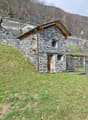 Stone house, wooden roof, wooden door, two windows, located on a slope