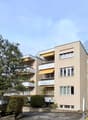 4 story building, beige exterior, multiple balconies, awnings, greenery