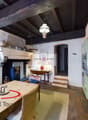 Rustic kitchen with exposed wooden beams, stone walls, and a fireplace. The kitchen features a wooden dining table, wicker chairs, and various kitchen appliances and utensils. There is also a 360 degree virtual tour sign visible.