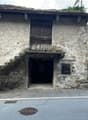 Two-story stone house, wooden staircase, dark entrance, stone walls, two cars parked on the road
