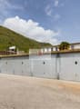 Garage building with multiple storage units, concrete floor, sign reading 'ABETE ROSSO Immobiliare', surrounded by greenery and a mountain in the background