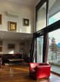 Spacious living room with large windows offering a scenic view, hardwood flooring, leather sofa and armchair, framed artwork on the walls, and air conditioning unit