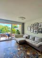 modern apartment living room, L-shaped couch, carpet, floor to ceiling windows, large balcony, trees view