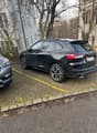 Black Kia Sorento SUV parked on the street, with a grey car parked next to it. The SUV has a rear spoiler and large wheels.