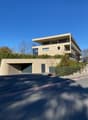 Modern architectural design, beige exterior, multiple levels, garage entrance, greenery on the roof, clear blue sky