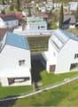 Modern white houses with solar panels on the roof, surrounded by a green lawn and a fence, aerial view