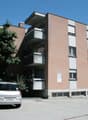 Multistory building, red bricks, several windows, balconies, parking in front
