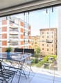 modern furnished balcony, large windows, view of other buildings, outdoor dining table and chairs