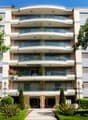multi-story building, balconies on every floor, entrance with arch, multiple plants and trees