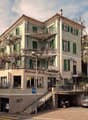 3-story building, white exterior, green shutters, balcony on first and second floor, awnings, restaurant on the ground floor, garage entrance