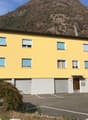 3 story yellow house, three garages in front, parking lot, mountain in the background
