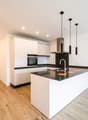 Empty modern kitchen with white cabinets, black countertops, wooden floor, oven, dishwasher, and sink with faucet.