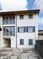 white building, 3 floors, multiple windows, balconies, stone pathway, stone wall