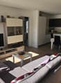 Gray couch, wooden floor, TV mounted on wall, dining table with chairs, kitchen island with black chairs, white walls, potted plant