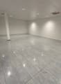 A room with white walls, ceiling, and tiled floor, and lights installed in the ceiling. There is a pillar in the middle of the room and an exit door at the right end.