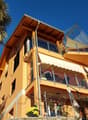 3 story house, yellow exterior, multiple balconies, glass railings, awnings, fenced yard