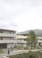 Modern apartment building, multiple floors, balconies, open green spaces, walking paths, trees, distant mountain