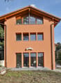 Two-story house, bright orange exterior, multiple large windows, black railing on balcony, located on a hillside