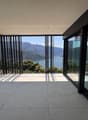 Large glass windows and sliding doors overlooking a scenic lake and mountain landscape, with a spacious outdoor terrace or balcony area.