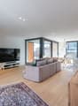 L-shaped gray sofa, large television, wooden floor, large windows, balcony, large mirror, wooden console table, flower vase, rug