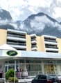 A multi-story commercial building with a parking lot in front, located in a mountainous area with clouds and fog in the background.