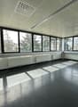 Large open office space with floor-to-ceiling windows, suspended ceiling with ventilation grilles, and concrete flooring. The space appears to be empty and ready for use.
