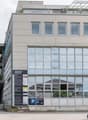 4-story commercial building with a glass facade, balconies on the top floor, and a parking area in front of the building