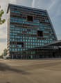 Modern high-rise building with glass facades, large triangular design, multiple entrances, surrounded by trees and concrete parking lot, signage reading UPTOWN