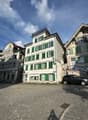 3 story building, white exterior, green shutters, cobblestone street, parked car