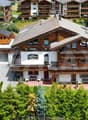 large chalet style house, wooden exterior, multiple balconies, parking area, garden