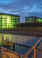 modern building with green glass walls, raised ground floor, metal railings, green roof