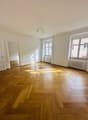 An empty room with parquet flooring, white walls, three windows, and two radiators. One of the rooms has a mirror.