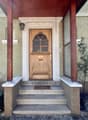 Wooden entrance door with glass windows, wooden pillars, stone stairs, plants