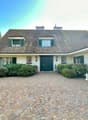 traditional style house, green front doors, brick driveway, green garage doors, lamps, bushes, statue, trees in the background