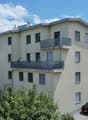 3 story building, beige exterior, multiple balconies, parking area, trees, shrubs