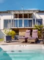 hot tub, lounge chairs, umbrella, plants, wooden deck, house in background