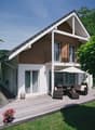 Detached house, 2 stories, brown and white, glass windows, wooden deck, chairs and table, umbrella, flower pots