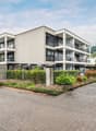 Modern apartment building with balconies, brick walls, paved driveway, greenery
