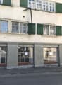 Storefront with green shutters, several windows, ground floor, two floors, sign on the left, three glass doors in front