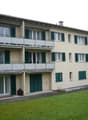 3 story apartment building, beige walls, green shutters, balcony on the top floor