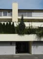 2 story house, white exterior, raised ground floor, garage, balcony, green roof