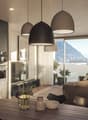 The image shows a modern, open-plan living room and kitchen area with large windows offering a scenic view of the surrounding mountains. The kitchen features dark, minimalist cabinets and appliances, while the living room has a comfortable brown sofa and