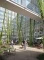 This image shows a large glass and steel commercial building with a lush, green indoor atrium. The atrium features hanging vines and plants, creating a natural and relaxing environment. There are people sitting at tables and chairs, suggesting this is a p