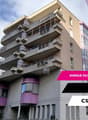 Apartment building, beige walls, purple balconies, multiple windows, street level entrance, parking