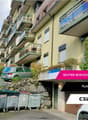 apartment building, multiple balconies, cars parked, trash bins