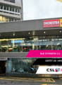Building located at Rue St-Martin, 1003 Lausanne. Large entrance with glass walls, staircase, glass doors, and storefront with an escalator. A shop sign for 'ORCHESTRA' and 'King Jouet' is present on top. Address and real estate information displayed on t
