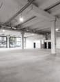 large open space with concrete floor, glass walls, exposed ceiling beams, visible parking area