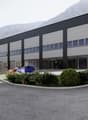 Modern warehouse, gray exterior, large windows, several parking spaces, landscape with shrubs and flowers, mountains in the background